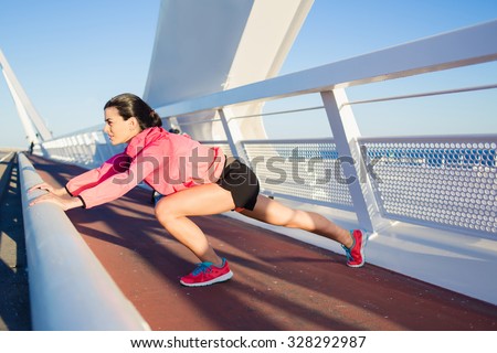 Portrait of young athletic female with a beautiful slender figure stretching muscles before began her evening run in the fresh air, fit woman with perfect body working outdoors during recreation time