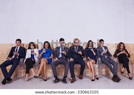 Full length portrait of International group of young intelligent lawyers chatting on they mobile phones, confident business people dressed in office clothing using cell telephones before start meeting
