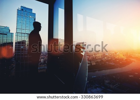 Silhouette of young intelligent man managing director resting after late business meeting while standing near big office window background with copy space for your text message or promotional content