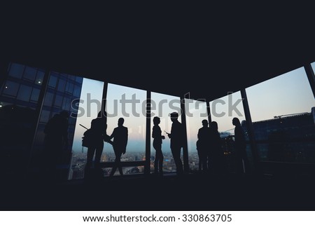 Silhouette of group of young skilled business people talking among themselves while standing in modern office interior near window, mans and women\'s purposeful bookkeepers discuss ideas after meeting