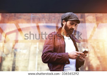 Portrait of a stylish adult men chatting on mobile phone while standing on the street in cool autumn day, fashion male with trendy look using his mobile phone during strolling in urban setting