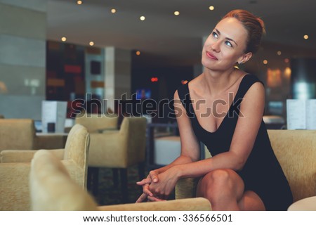 Portrait of a charming successful female entrepreneur thinking about new business ideas while sitting in modern interior, young dreamy prosperous woman in formal wear enjoying rest after work day