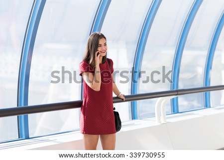 Half length portrait of a happy stunning woman having a telephone conversation while standing in modern interior, young gorgeous female with cute smile talking on smart phone with her best friend