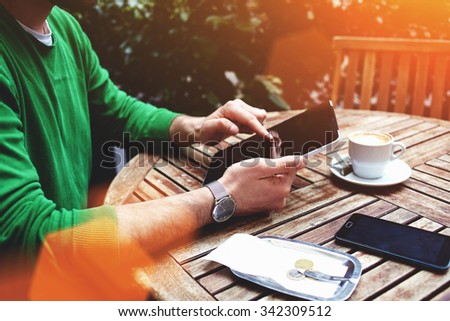 Cropped shot view of a man\'s hand keyboarding on touch pad while sitting in sidewalk cafe in summer day, male freelancer using digital tablet for remote work during breakfast time in sidewalk cafe