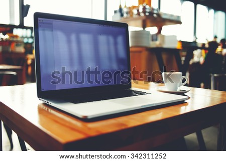 Portable net-book with copy space screen for your text massage or promotional content, open laptop computer and cup of hot drink lying on a wooden table in cafe interior, freelance work in internet