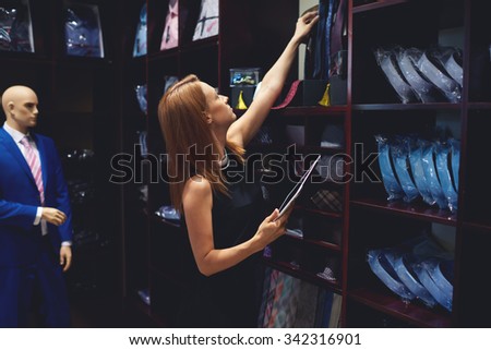Portrait of a businesswoman checks availability of goods by using the touch pad while standing in her modern shop, young female consultant holding digital tablet during work in fashionable boutique