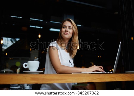 Young gorgeous European woman with pretty face thinking about something while sitting with laptop computer in cafe bar, dreamy beautiful female using portable net-book during work break in coffee shop