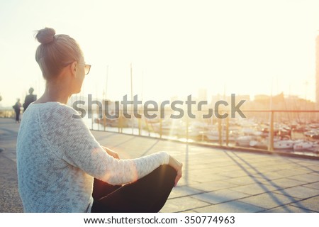 Young hipster girl enjoying sun and good warm day during her recreation time, woman relaxing outdoors after walking in the fresh air, female looking at the landscape while sitting near sea port