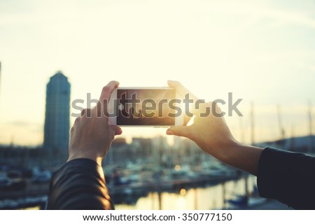 Cropped shot view of woman\'s hands making photo on mobile phone camera of building against beautiful sunset, hipster girl photographing on cell telephone wonderful landscape during strolling outside