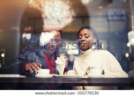 Dark skinned man and woman sitting together in coffee shop interior while rest after walking outdoors and drink cafe, two friends relaxing after strolling in cold winter day during weekend