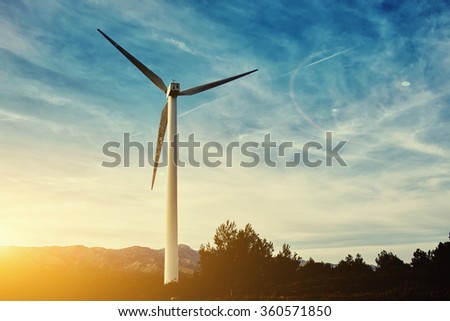 Beautiful sunset behind the windmill on the field, electric generator against cloudy sky background with copy space, renewable energy sources, wind turbine location in field