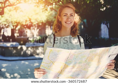 Beautiful happy female tourist exploring location map before touring in a city during her travel, young female traveler with cute smile studying new way on atlas during amazing summer adventure