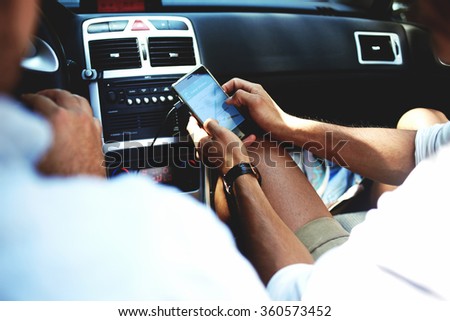 Cropped shot view of a young man using navigation on mobile phone while sitting on front seat in luxury car cabriolet, male viewing location map in network via cell telephone during road trip