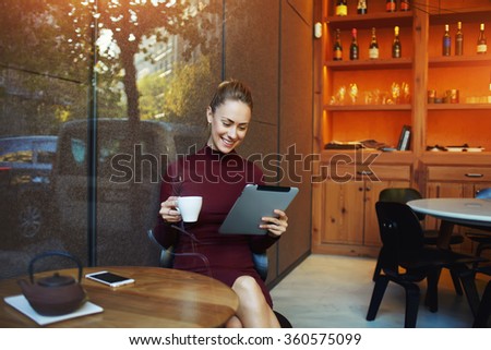 Young charming woman have video Ã?Â?Ã?Â�hat with sister via digital tablet while sitting in her favorite cafe drinking delicious green tea, female watching movie on touch pad while breakfast in coffee shop