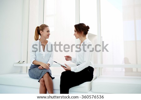 Two young successful female managing directors using digital tablet while discuss new business ideas, confident woman lawyers holding portable touch pad while talking with her clients in modern office