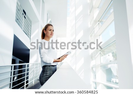 Thoughtful woman holding digital tablet and looks into the window after business meeting with partners, young successful female financier ponders over the future of company during work break in office
