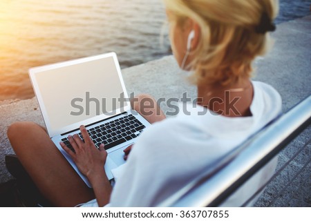 Back view of female using net-book with blank copy space screen for your text message or promotional content, young woman reading news via laptop computer while sitting near sea during her vacations