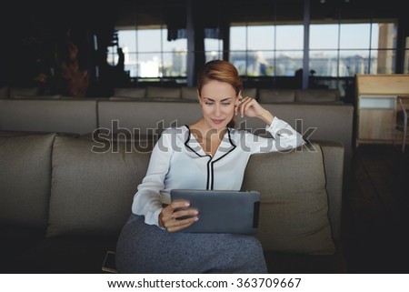 Confident woman ceo reading information on portable touch pad while waiting for start meeting with business partner,young female watching news via network on digital tablet while sitting in restaurant