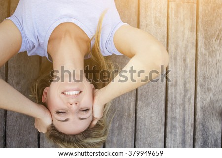 Upside down image of a young blonde woman with beautiful smile lying on a wooden floor in the fresh air, happy cheerful hipster girl posing for camera with copy space for your advertising text message