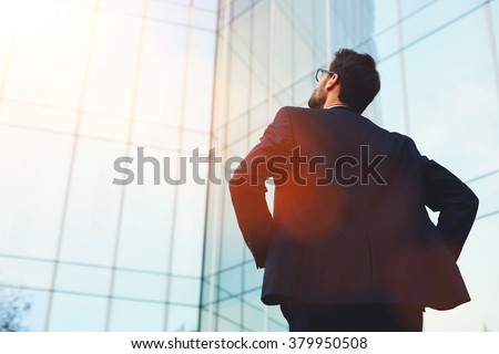 Back view of male architect looking on designed by him modern bank building while standing outside, intelligent young businessman dreaming about prosperity of his company after important meeting