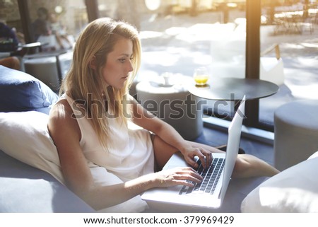 Young woman writer keyboarding text for a new book via laptop computer while sitting in co-working cafe,pretty female student searching information on net-book during lunch break in modern coffee shop
