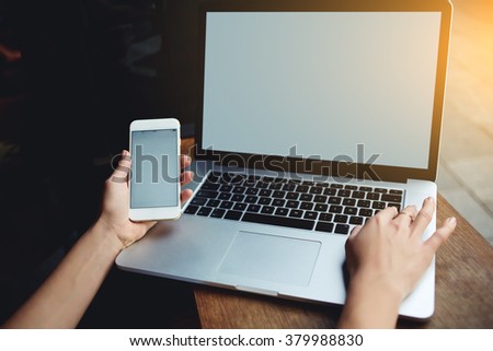Closeup of women\'s hands using mobile phone and laptop computer with blank copy space screen for your advertising text message or content, female holding cell phone and keyboarding on net-book