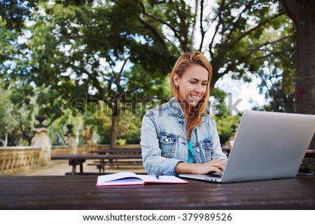 Young smiling woman student using portable laptop computer for preparation to exams at the University, happy Caucasian female keyboarding on net-book while sitting in beautiful city park in spring day