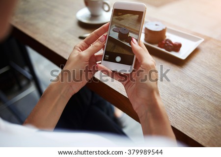 Closeup of women\'s hands making photo of sweet dessert on mobile phone while sitting in comfortable restaurant, female taking pictures with cell phone camera of delicious pastry during rest in cafe