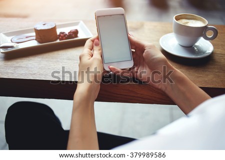 Close up of women's hands holding mobile phone with blank copy space screen for your advertising text message or promotional content, female reading news on cell telephone during rest in coffee shop