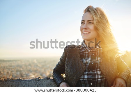 Young attractive woman with good mood enjoying beautiful city landscape while standing on a roof of building, charming smiling hipster girl relaxing after excursion during her amazing spring weekend