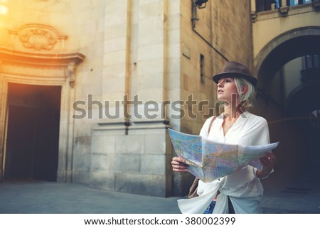 Beautiful woman traveler holding location map in hands while looking for some direction in urban scene in sunny summer day, young female student checking out the sights on atlas during trip overseas