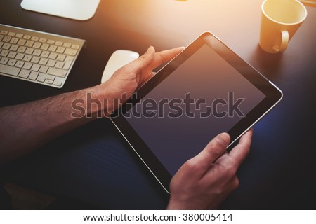 Closeup image of man\'s hands holding digital tablet with blank copy space screen for your text message or promotional content against desktop with wireless keyboard, computer mouse and cup of tea
