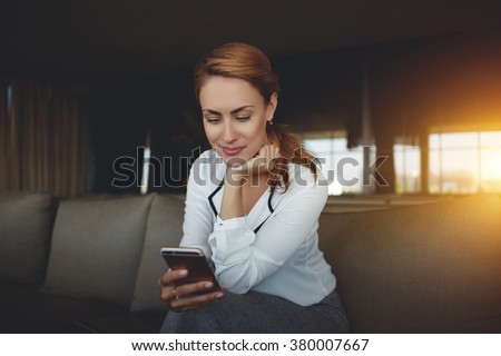 Beautiful female reading on mobile phone text messaging from her boyfriend while sitting in comfortable coffee shop interior, young businesswoman watching world news on cell telephone before meeting