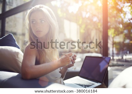 Successful woman restaurant owner holding cup of coffee and looking for new customers who came on a lunch, beautiful female enjoying hot beverage while resting after work on portable laptop computer