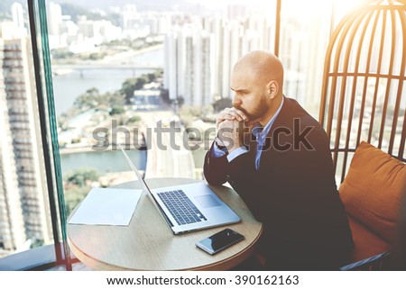 Concentrated and worried businessman sitting front open net-book in his office, male entrepreneur reading the financial breakdown of his budget while using laptop computer during work day in company