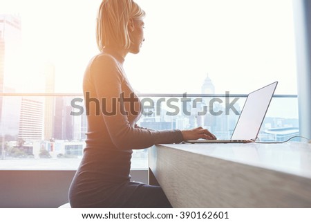 Young woman journalist is looking thought window while is thinking about writing of the text for magazine article. Female student is keyboarding on laptop computer while sitting in university library
