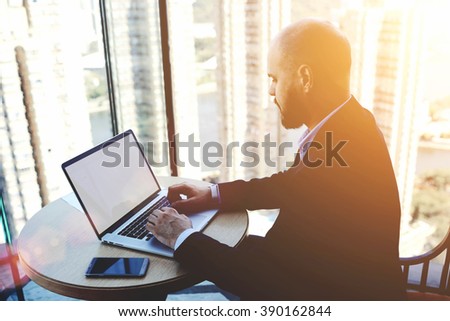 Experienced man trader is analyzing financial market via laptop computer, while is sitting in modern office interior. Male skilled accountant is checking the validity of the operation via net-book