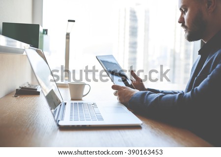 Closely of a man proud economist is searching information on touch pad for preparing meeting with staff. Successful business worker is using digital tablet, while is sitting at the table with net-book