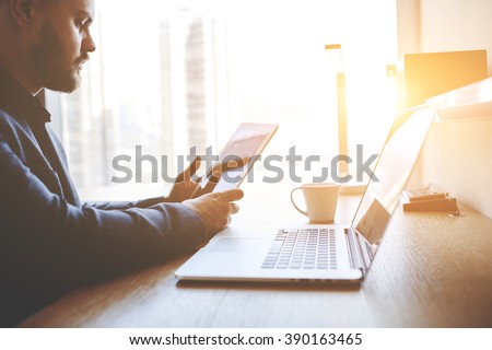 Closeup of a serious man office worker is reading world news in internet on touch pad, while is sitting at the table with open net-book. Closely of a successful male lawyer is using digital tablet
