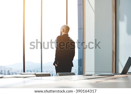 Back view of young confident man leader is resting after business meeting with foreign partners, while is standing near big office window background with copy space for your advertising text message