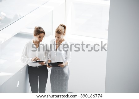 Young women leaders are checking financial statements from paper documents and portable touch pad. Two female confident business worker are using digital tablet for preparing to conference with staff