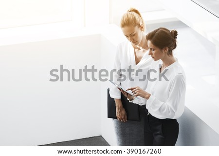 Two female professional bankers are watching condition currency on Exchange via touch pad, while are standing in office interior near copy space. Women successful economists are using digital tablet