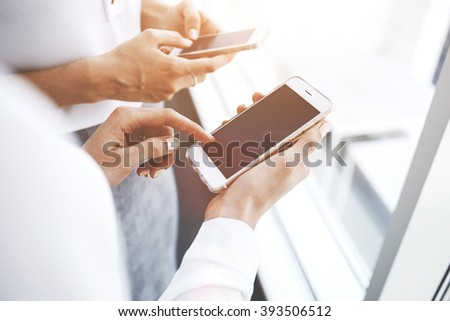 Close up image of woman`s hand is touching finger of mobile phone screen, while her partner is typing text message on cellphone. Two female students are searching on cell telephones information
