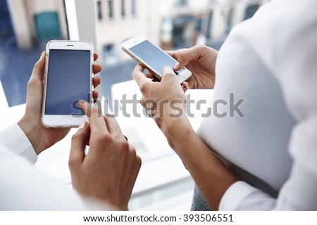 Closeup image of businesswoman pointing the finger on a copy space on the screen mobile phone for your advertising text message or promotional content, while her secretary near is using cell telephone