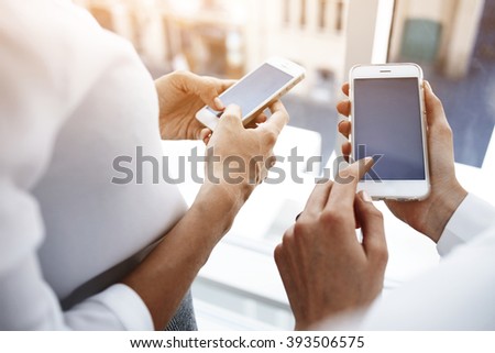 Closely image of woman`s hand is holding cell telephone with copy space screen for your advertising text message, while her friend near dials the number on smart phone. Two female are using cellphones