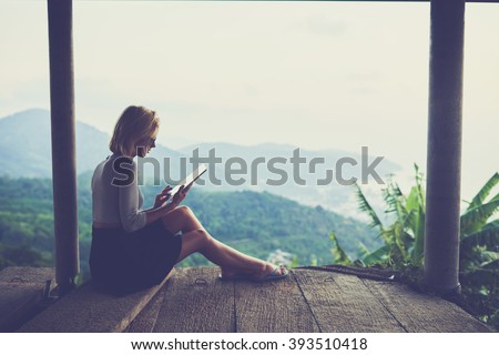 Woman freelancer is working on distance via portable digital tablet, while sitting against wonderful jungle scenery background with copy space for your advertising text message or promotional content