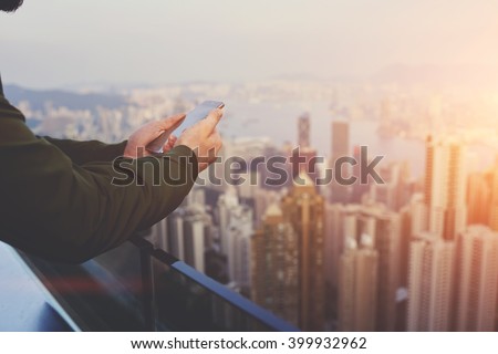 Closely of man successful broker is using mobile phone,while is standing on building roof against view of New York city with tall skyscrapers. Hipster guy is connecting to internet via cell telephone