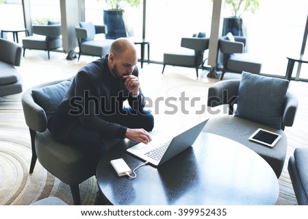Confident businessman is reading in network via laptop computer customer reviews about his company. Male successful lawyer is studying dealing new client by using net-book, while is sitting in cafe