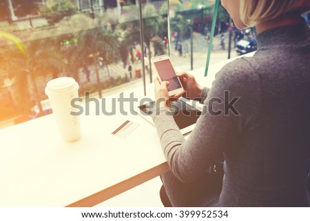 Woman is chatting on mobile phone, while is sitting in cafe at the table with digital tablet, credit card and take away coffee. Female is booking restaurant for dinner on-line via cell telephone