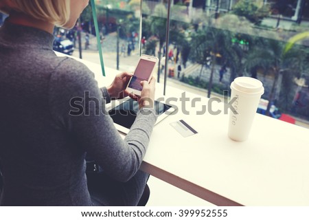 Closely of woman is typing text message on cell telephone, while is resting in coffee shop of modern shopping center in New York. Young hipster girl is chatting in social network via mobile phone